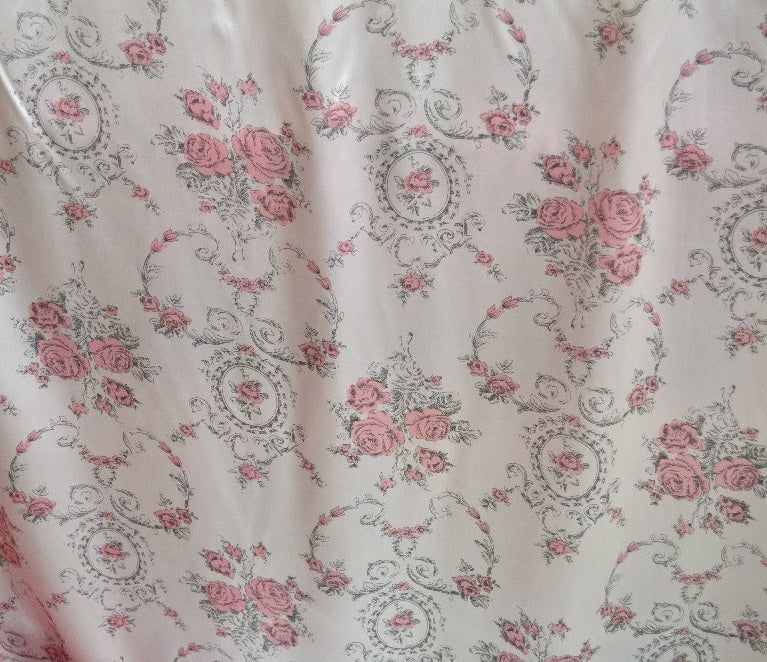 Floral patterned fabric with pink roses and decorative swirls on a light background