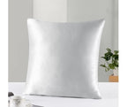 Silver satin pillow on a white surface with a neutral background