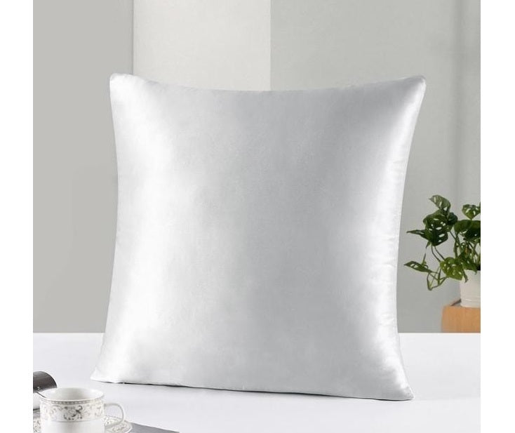 Silver satin pillow on a white surface with a neutral background